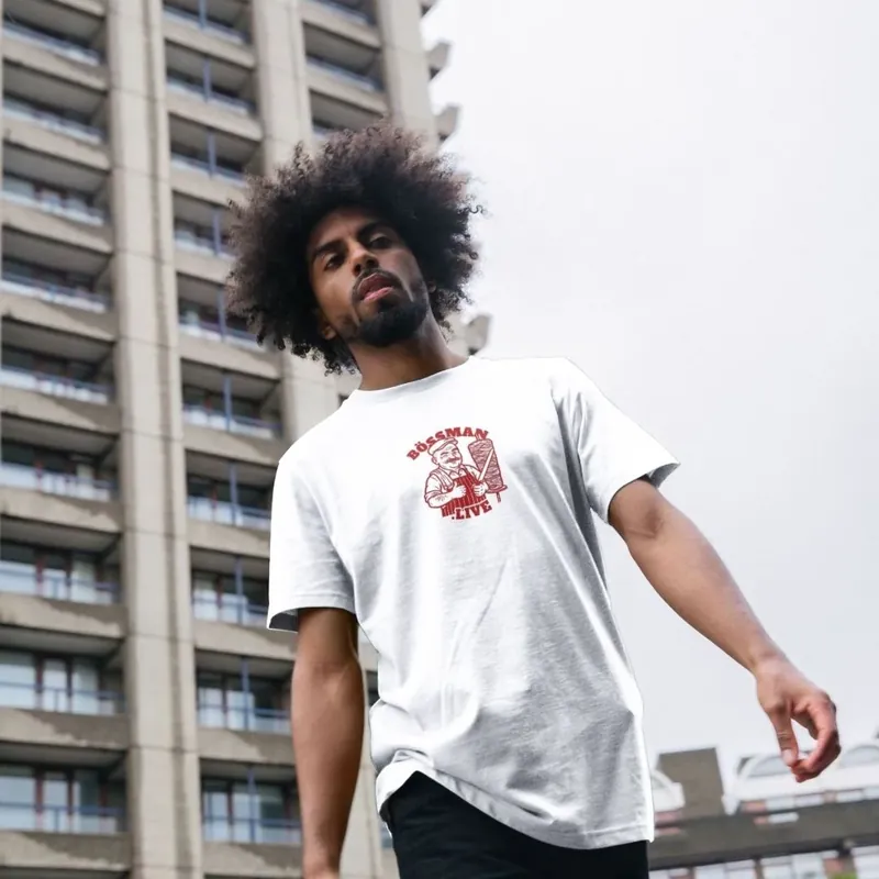 A man wearing the white Bössman tee outside a tower block, with the small red Bössman.live print on his chest